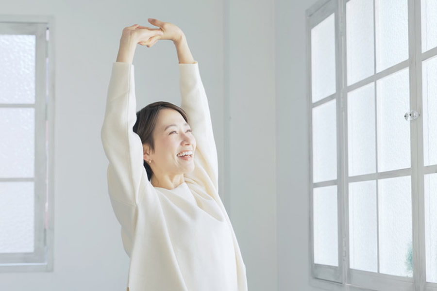 窓際で背伸びをして笑顔の女性