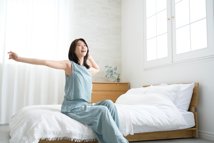 ベッドの上で手を上げてストレッチをしている女性