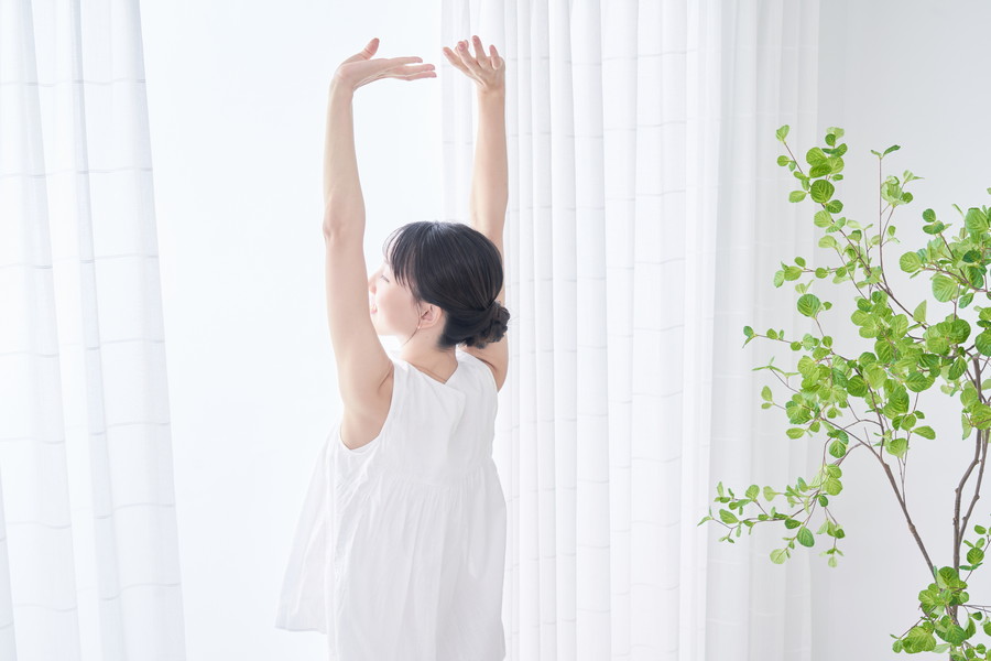窓際で朝日を浴びて背伸びをしている女性