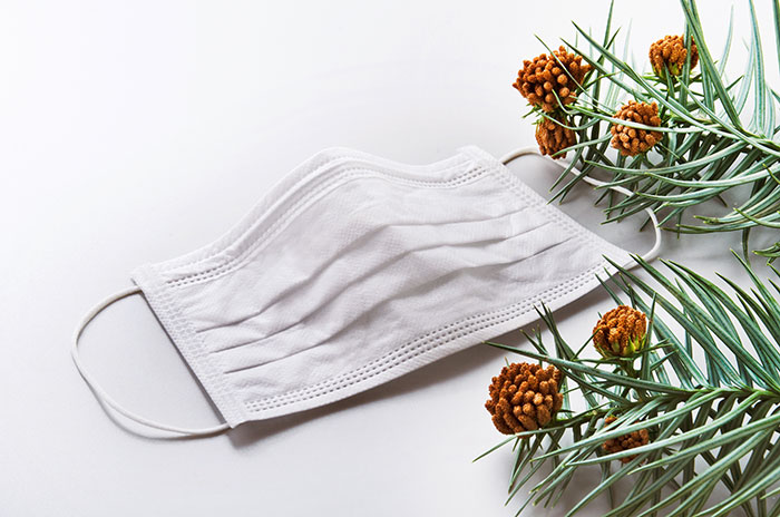 白いマスクと花粉を含む針葉樹の枝が並んだ、花粉対策をイメージした画像