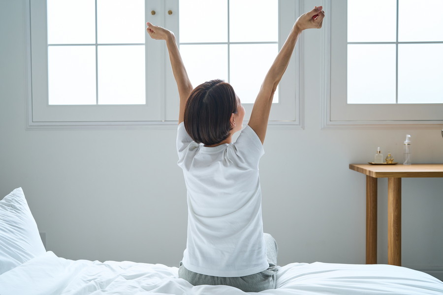 ベッドに座って背伸びをしている女性